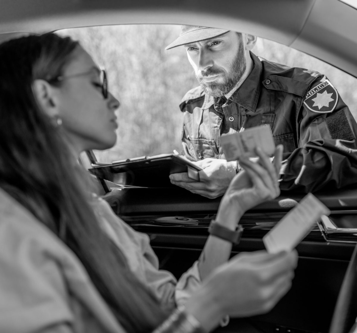 Policeman checking documents of a young female driver sitting in the car, view from the car interior